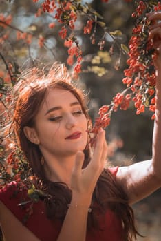 young girl picking red berries from a branch in autumn. she has long hair and a nice smile close-up
