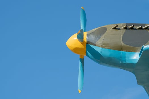 A close-up view of a vintage aircraft's propeller showcasing its colorful design. The bright yellow hub and blue blades stand out against the clear blue sky during daylight.