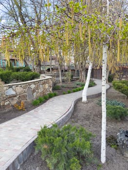 A winding garden path showcases vibrant blooms and lush greenery in a peaceful outdoor area. The landscaping features stone walls and a variety of plants under clear skies.