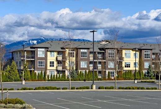 Low rise residential building with big parking lot in front on mountain and cloudy sky background