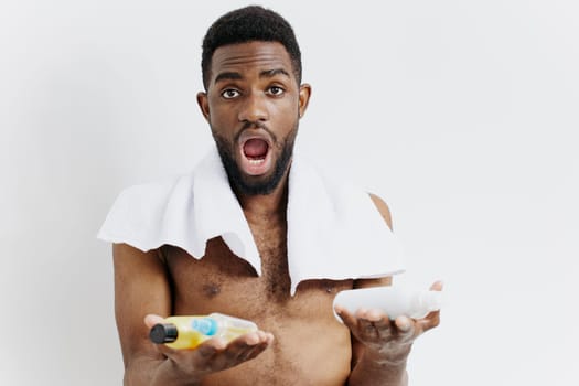 Shirtless man emphasizes self-care routine holding lotion and toothpaste in a sleek, minimalistic bathroom setting.