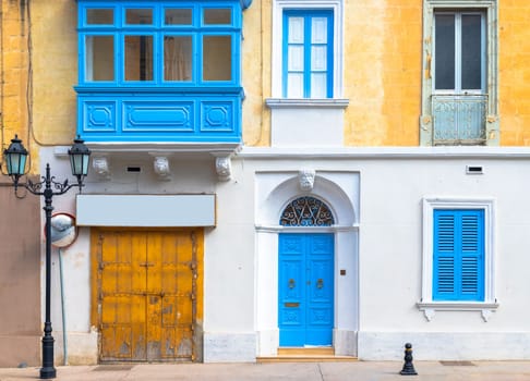 Facade of a traditional Maltese building with balcony, shuttered windows and garage gate.