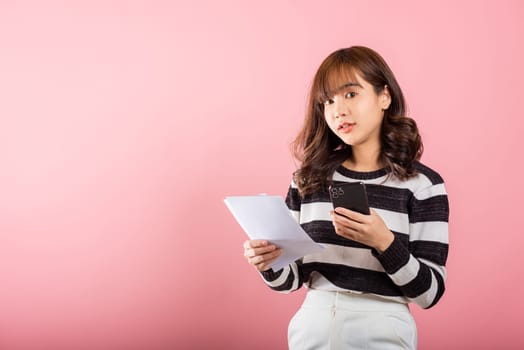 Happy Asian young woman holding mobile smart phone and family budget cost bills document invoice online for payment, Convenience online internet banking. female hold work papernote