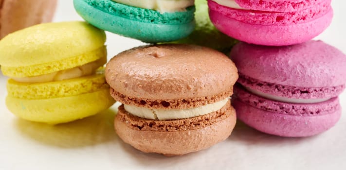 An assortment of colorful macarons on a white surface. The macarons have a smooth, delicate shell and a creamy filling