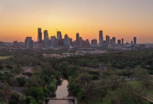 Brilliant orange and red sky behind the illuminated city skyline of Austin Texas at dawn over Barton creek pool