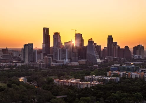 Rising sun appears between the skyscrapers of Austin, Texas at dawn in aerial view from Zilker park