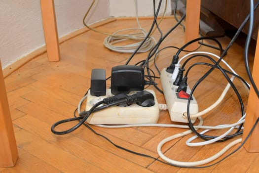 Cable chaos clutter from multiple electric wire extension cords and multi-contact plugs on wooden floor. Tangled cables on the parquet floor