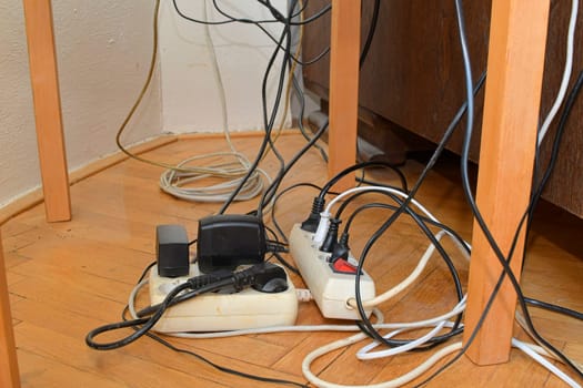 Tangled cables on the parquet floor. Overloaded electrical boards on the wooden floor. Electrical cables in disorder