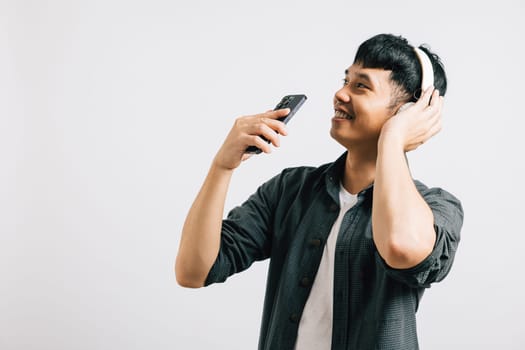 A young Asian man, positively immersed in karaoke, sings along to music on his smartphone with Bluetooth headphones. Studio shot isolated on white background, capturing his joy.
