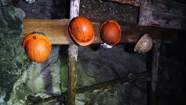 Four colorful miners' helmets hanging on a weathered wooden beam in an abandoned mine evoke memories of past labor and industry, highlighting the rich history of resource extraction
