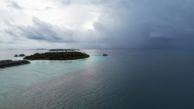 Aerial view of a luxury resort in the maldives with overwater bungalows and a pristine beach, as dark storm clouds gather in the distance, creating a dramatic contrast