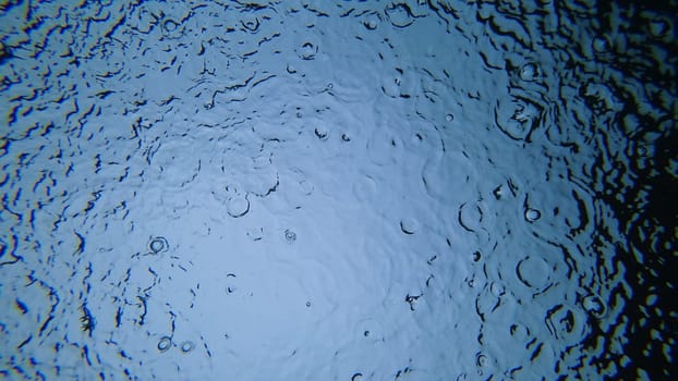 Rain droplets falling on a tranquil blue water surface, creating mesmerizing concentric circles and gentle ripples, offering a calming and meditative atmosphere for relaxation