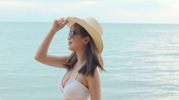 Beautiful Asian woman wear sungrass and hat turning back to looking camera and smiling at beach, Portrait of happy female in bikini having fun laughing on tropical in summer holiday