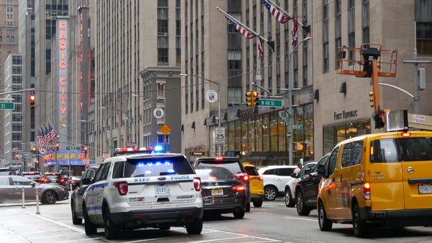 New York, United States - 10 Sept 2023: Police patrol car, Radio City Music Hall. USA NYPD 911, Manhattan Midtown street. American cop auto siren light, 6 avenue. Urban road traffic scene. Yellow taxi