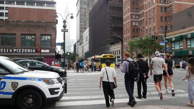 New York City, United States - 29 Aug 2023: Police patrol car, USA NYPD 911, Manhattan Midtown 34th street. American cop auto, 9 avenue. Urban road traffic. People, Empire State Building, yellow taxi.