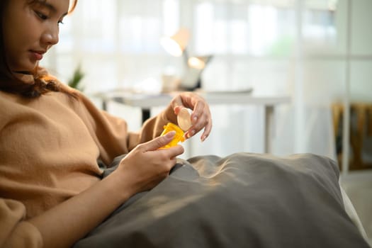 Young asian woman in casual clothes taking medicine while resting in a couch.