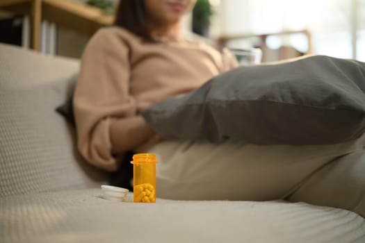 Prescription medicine bottle placed beside woman on sofa. Health care concept.