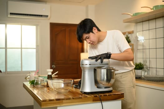 Young asian man preparing whipped cream with a stand mixer in home kitchen.
