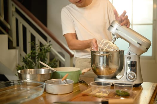 Young asian man using a stand mixer to whip cream in a bright modern kitchen.