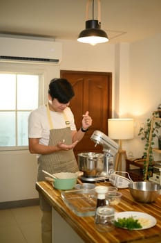 Young asian man using a stand mixer to whip cream in a bright modern kitchen.