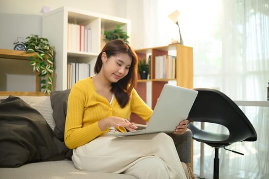 Young woman in yellow sweater working on her laptop in a bright living room.