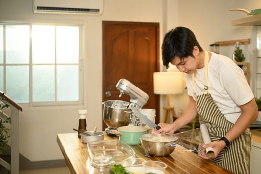 Young male baker wrapping whipped cream for storage.