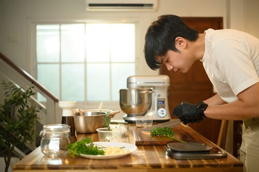 Close up of man chopping fresh herbs, preparing ingredients in a home kitchen.