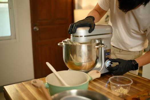 Young asian man preparing whipped cream with a stand mixer in home kitchen.