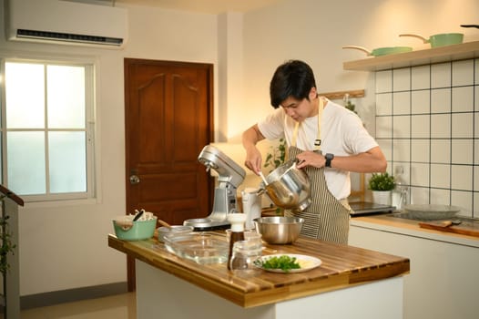 Young asian man using a stand mixer to whip cream in a bright modern kitchen.