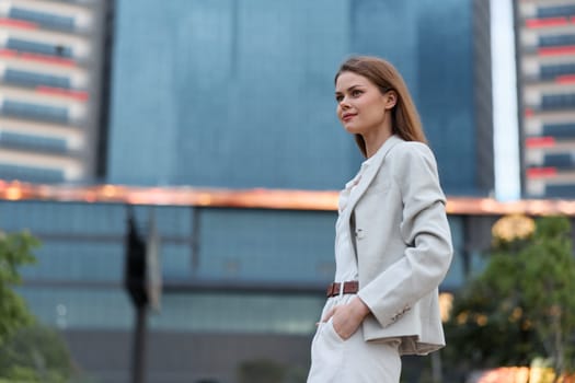 Confident woman in business attire standing outdoors in urban environment with modern buildings, showing calm and professional attitude, symbolizing business success and career growth.