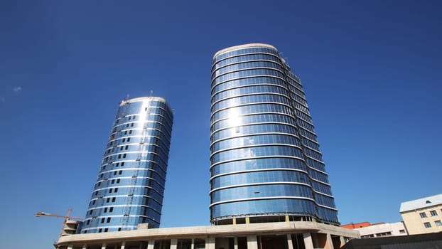 There are two extremely tall buildings standing prominently, and they are set against a beautiful blue sky that enhances their impressive stature
