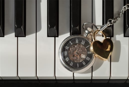 London, UK - Apr 19, 2025 - Antique pocket watch (A retro pocket watch) with Golden heart shaped love padlock on Piano keys background. The concept of the time of love, use it as your Wallpaper, Poster and Space for text, Selective focus.