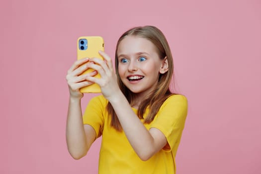 Excited girl with blue eyes in a yellow shirt taking a selfie against a pink background, reflecting happiness and joy, perfect for social media and lifestyle themes