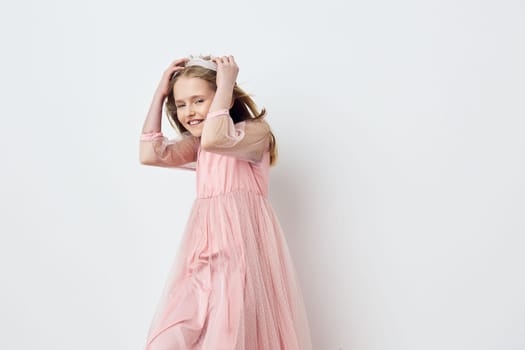 A joyful young girl in a flowing pink dress poses playfully against a clean white backdrop, radiating happiness and innocence Perfect for kids fashion or cheerful themes