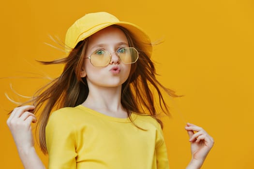 Cheerful girl wearing a yellow hat and glasses poses confidently against a vibrant yellow background This fashion forward image captures youthful joy and personality