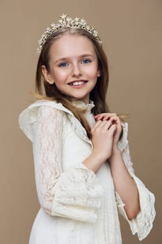 Charming young girl dressed in a beautiful lace gown and tiara, radiating happiness and innocence against a neutral beige backdrop Ideal for children s fashion and royalty concepts