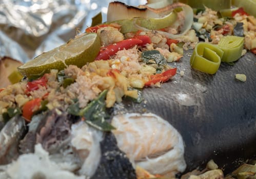 Close-up of Baked Salmon with Herbs, ingredient include Coriander root, Ginger, Galangal, Kaffir lime, Leek, chopped together and Bird's eye chili with Slice lemons place on the Salmon fish. Healthy eating, use it as your Wallpaper, Poster and Copy space, Selective focus.