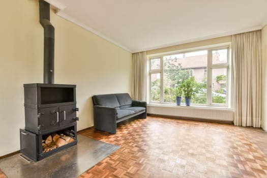 A warm and inviting living room featuring a wood stove, comfortable seating, and large windows that offer a view of greenery outside.