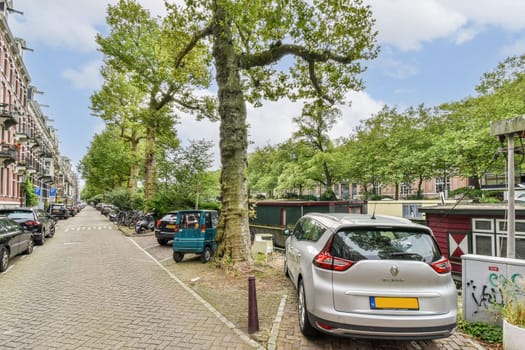 A tranquil urban street lined with green trees, various vehicles parked along the sides, and a scenic view of the surroundings.