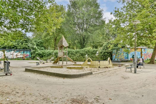 The scene features a playground with a play structure, benches, and colorful murals amidst tall trees and a bright sky, creating a lively atmosphere.