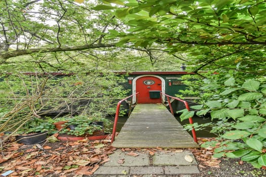A quaint entrance to a waterfront cabin surrounded by lush greenery and foliage. The wooden walkway invites visitors into a serene, natural environment.