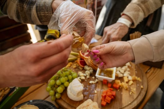 Cheese tasting at a farmers market, close-up of the hands of a seller and a buyer. The process of tasting cheese, the seller puts sauce on the cheese. Large assortment of natural products on the table