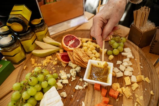 Cheese and fruit platter tasting at a farmers market. Close-up of a woman's hand tasting cheese and sauce with a wooden stick.