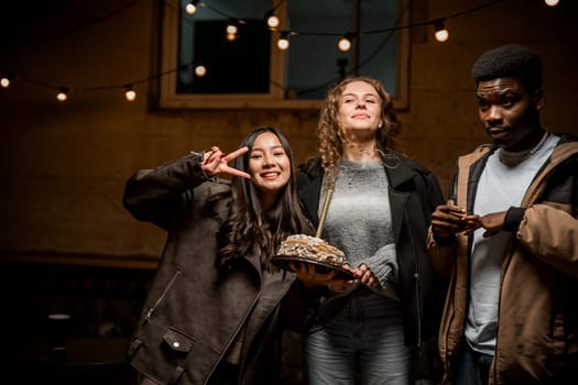 Three friends enjoy a joyful evening together in a cozy space. One holds a delicious cake, while the others smile and pose for a fun moment, embodying the spirit of celebration and friendship.