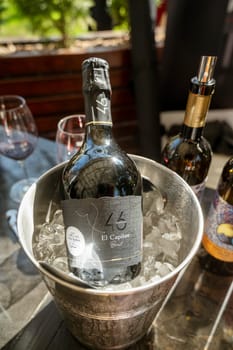Odessa, Ukraine - April 05, 2025: A bottle of champange in an ice bucket at a hotel outdoors on a spring day. In the background, a bottle of wine and glasses. The blurred background includes a wine glass