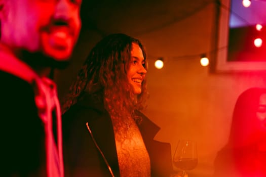 Cheerful friends gather indoors, enjoying drinks and laughter under colorful lights. The atmosphere is warm and inviting, perfect for a lively evening with good company.