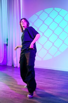 A dancer showcases creative movements in a well-lit studio, surrounded by purple and blue hues. The atmosphere is energetic and invites audience engagement.