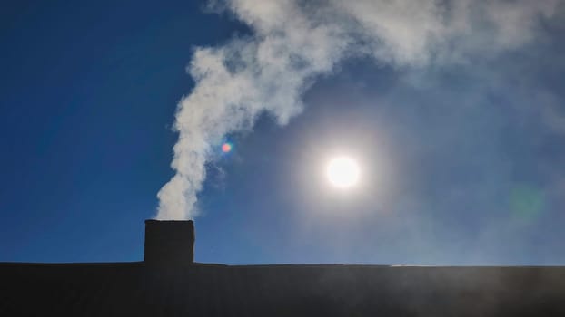 White smoke rising from a chimney on a sunny day, set against a backdrop of a clear blue sky, creates a cozy and inviting atmosphere