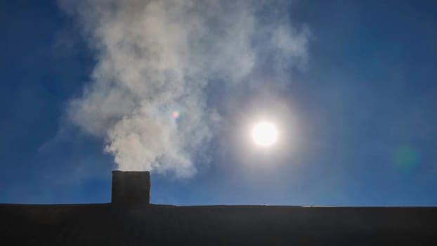 Smoke rising from a chimney against a twilight blue sky, casting a striking silhouette and evoking a sense of warmth in the evening air
