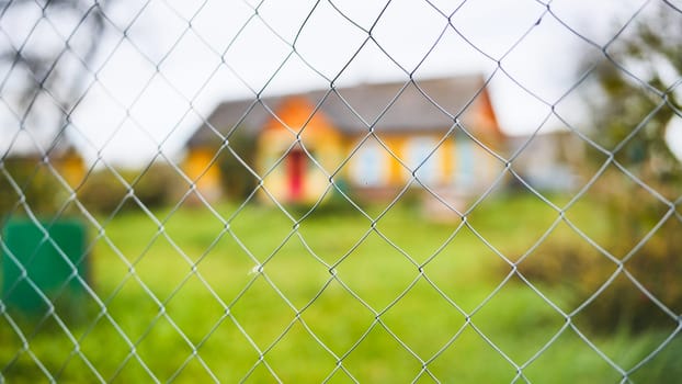 Close up of a chain link fence with a blurred house in the background, representing security, privacy, and property protection